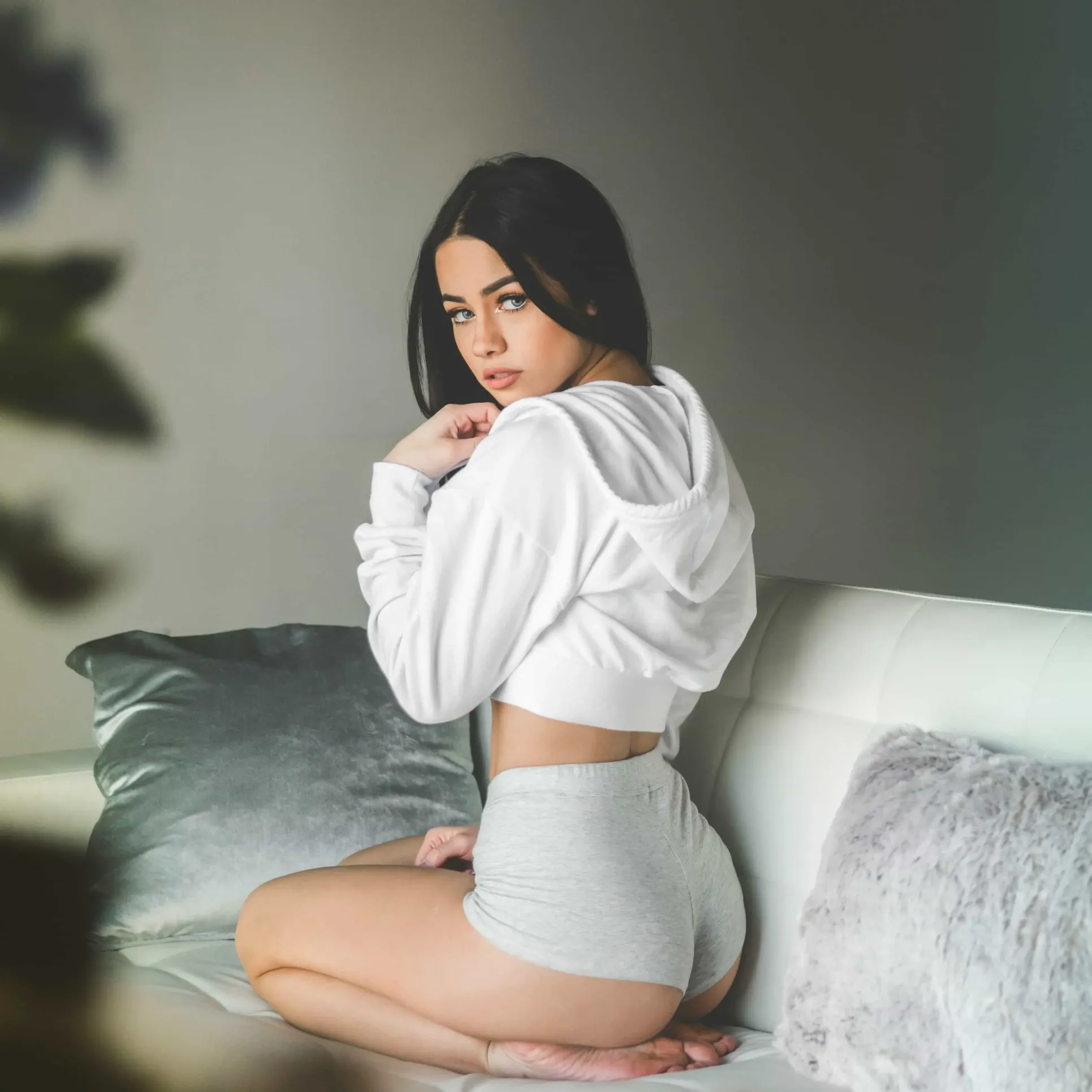 Young woman in grey used underwear and white hoodie on a sofa – intimate and sensual image representing used underwear for sale on Bamboo Black Coffee